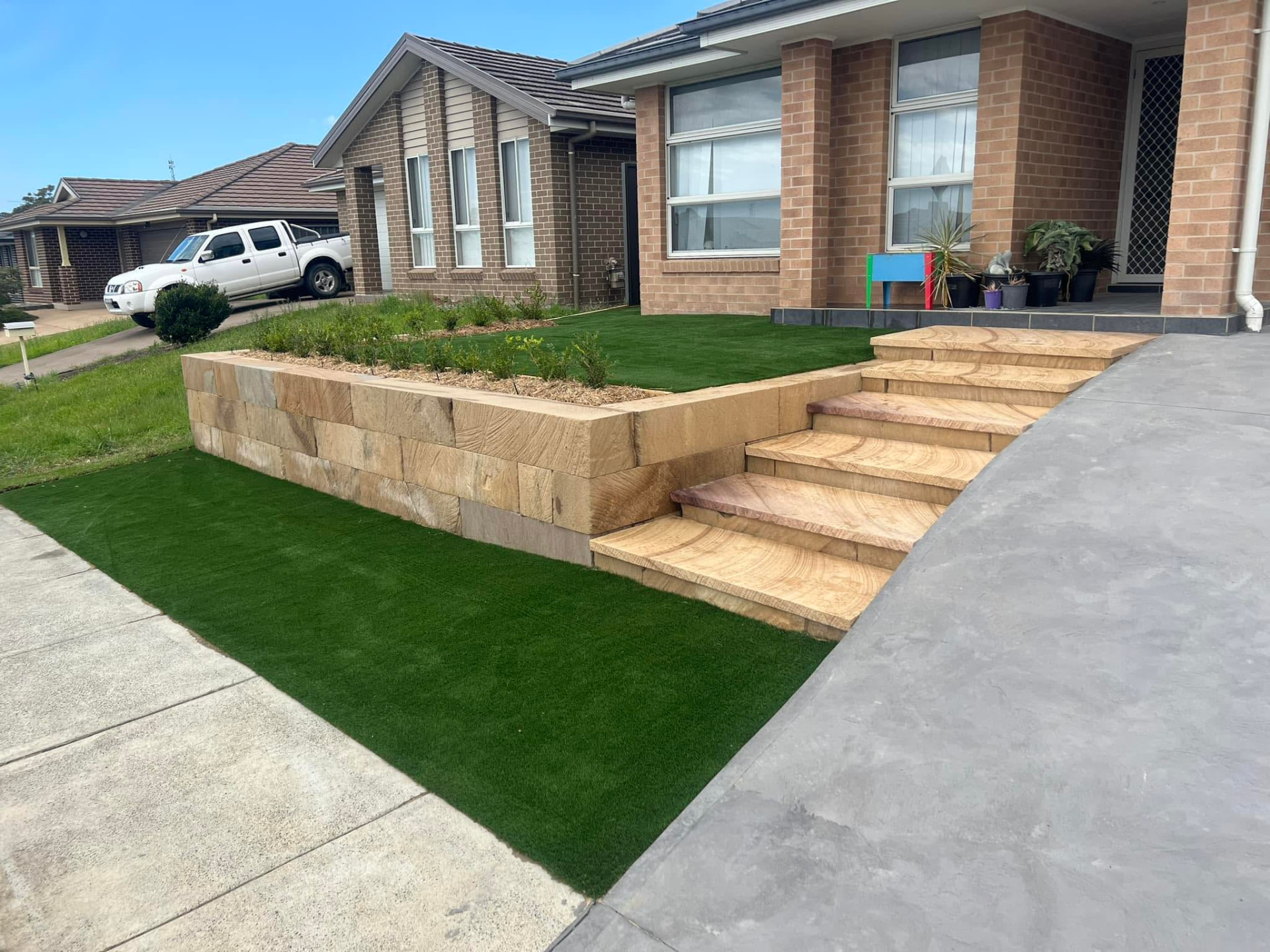 Sandstone retaining wall and stairs leading up to a modern brick home