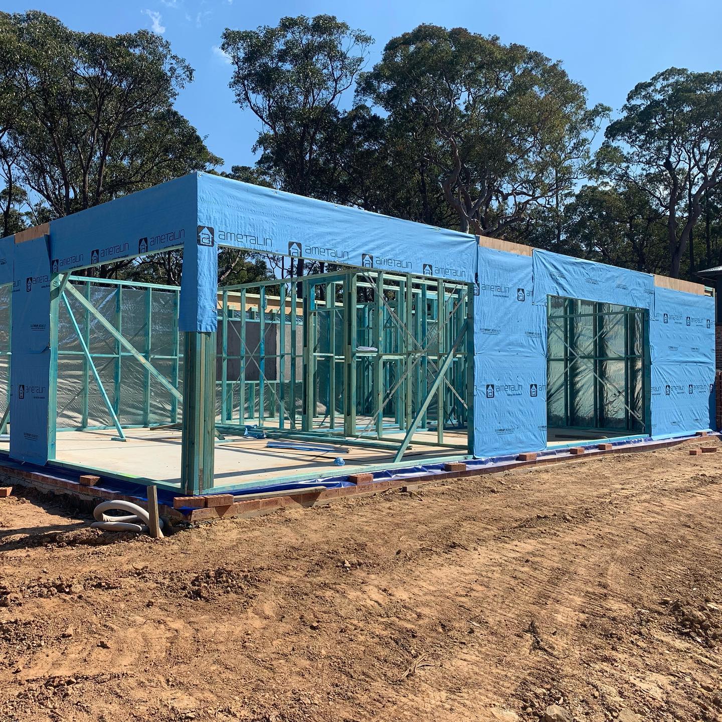 Timber framed home wrapped in blue building wrap on a bush block