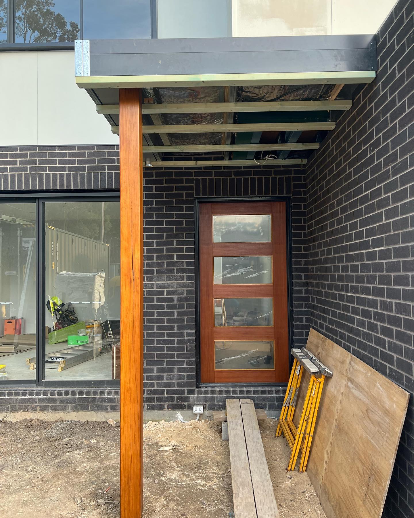 Timber post and framed portico over the front entry of a dark brick home