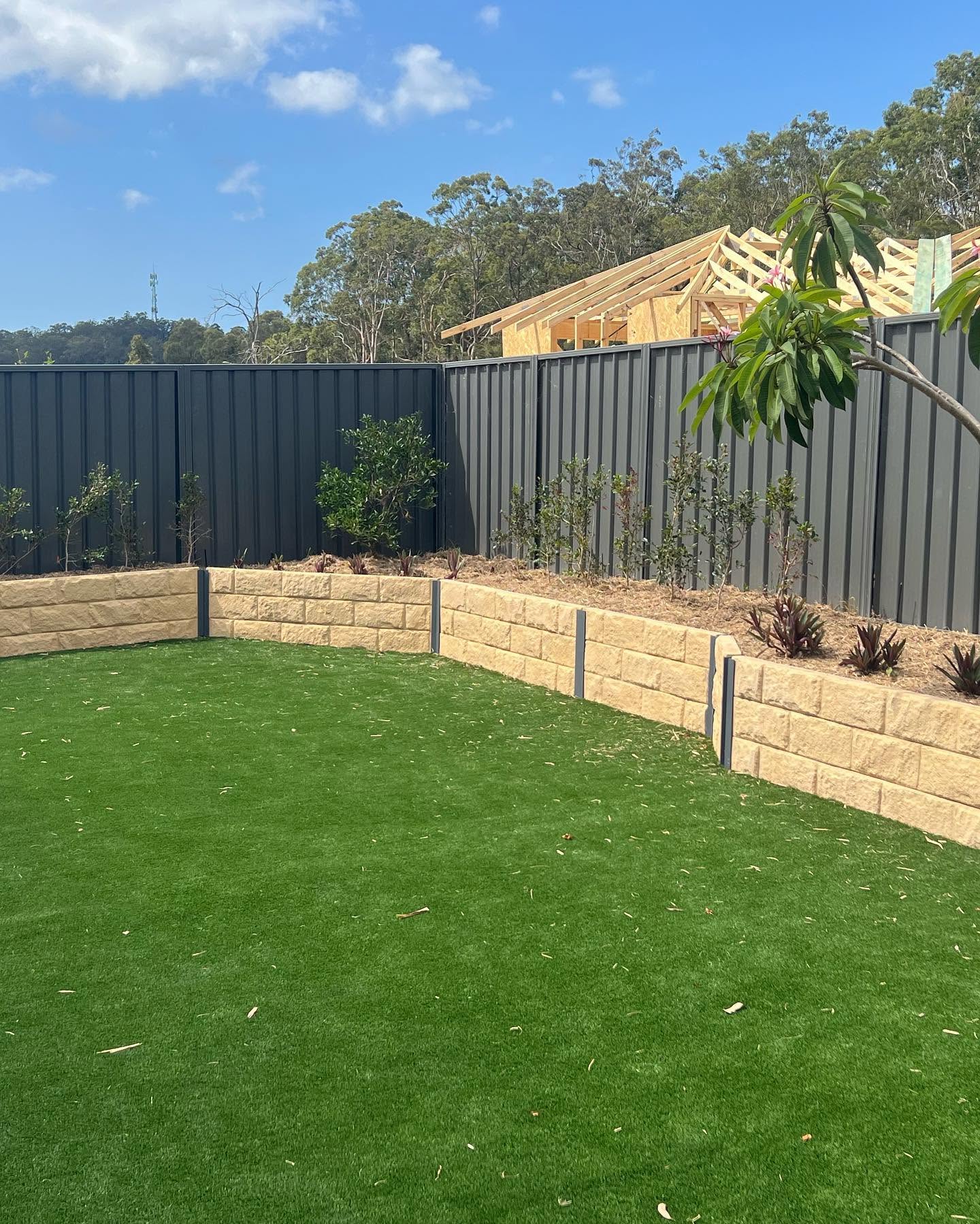 Backyard with sandstone retaining wall, artificial turf and dark metal fence
