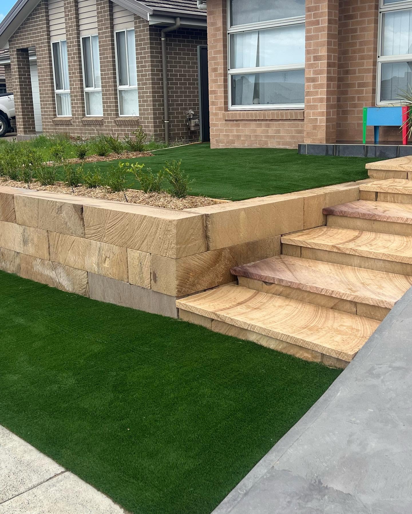 Completed sandstone block retaining wall with matching stairs beside a lawn