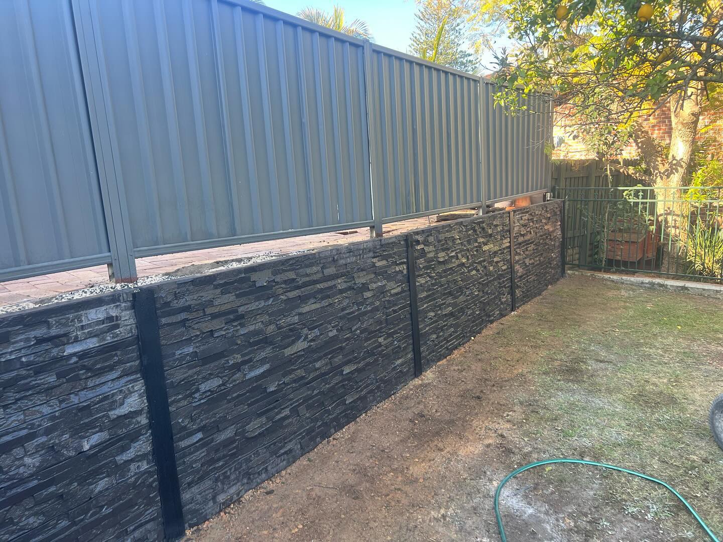 Charcoal stacked stone retaining wall along a backyard boundary